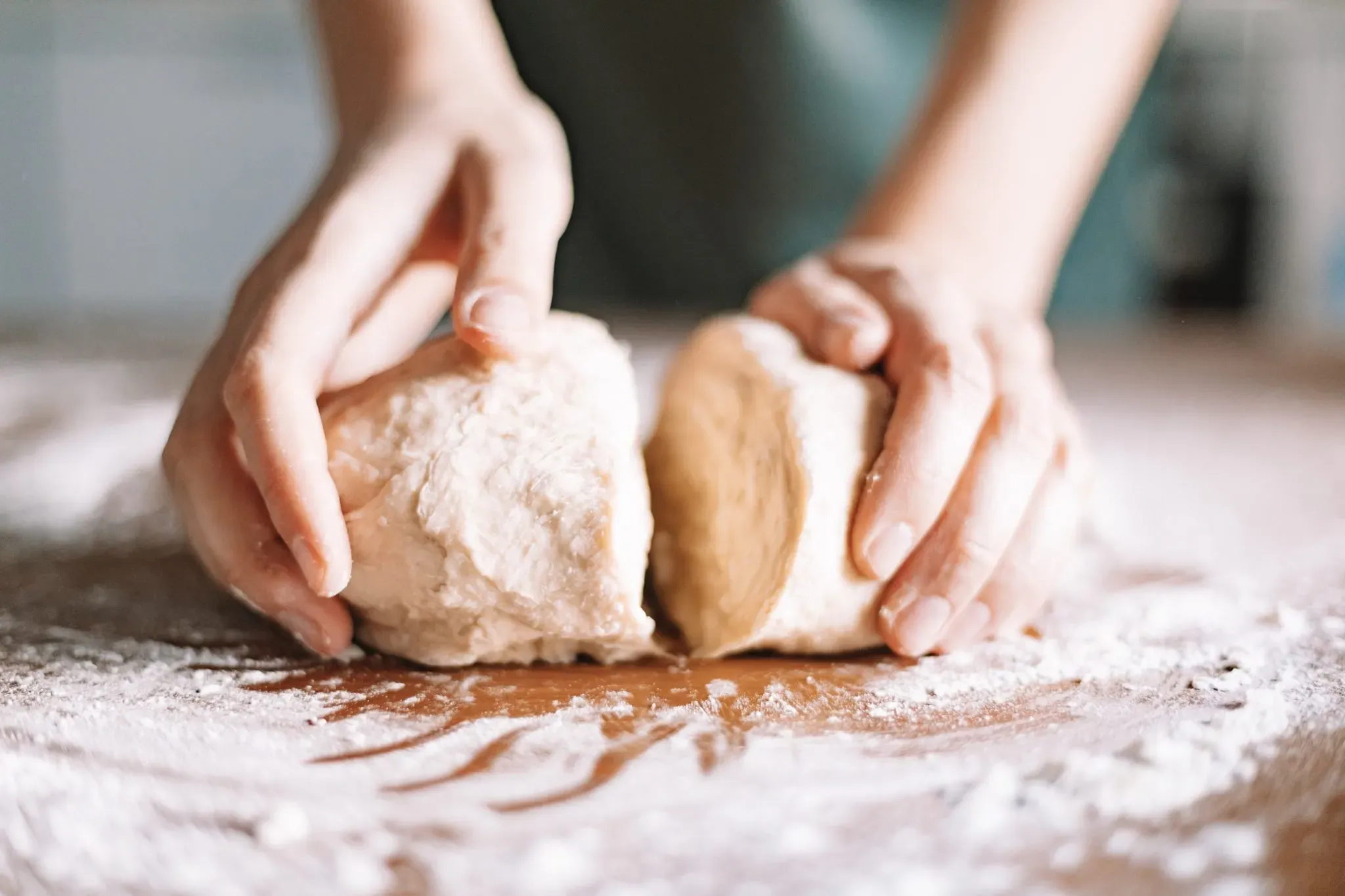 Mani che dividono un impasto di pane su un piano infarinato